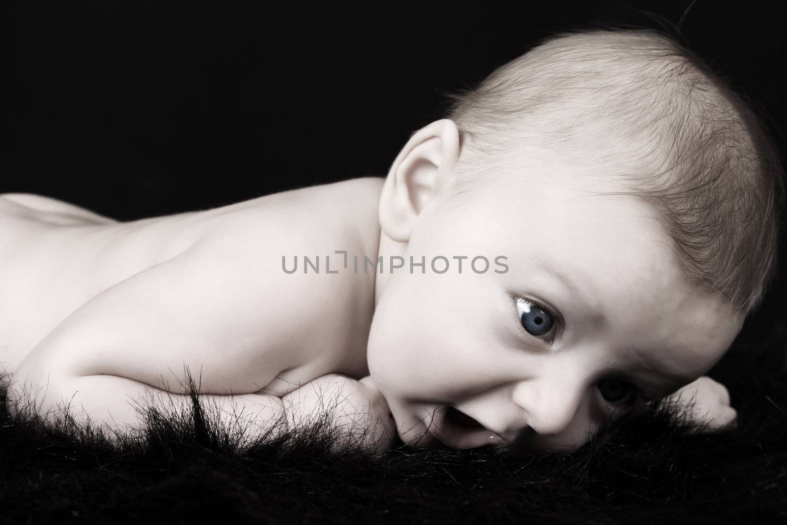 Beautiful three month old baby boy lying on black fur 