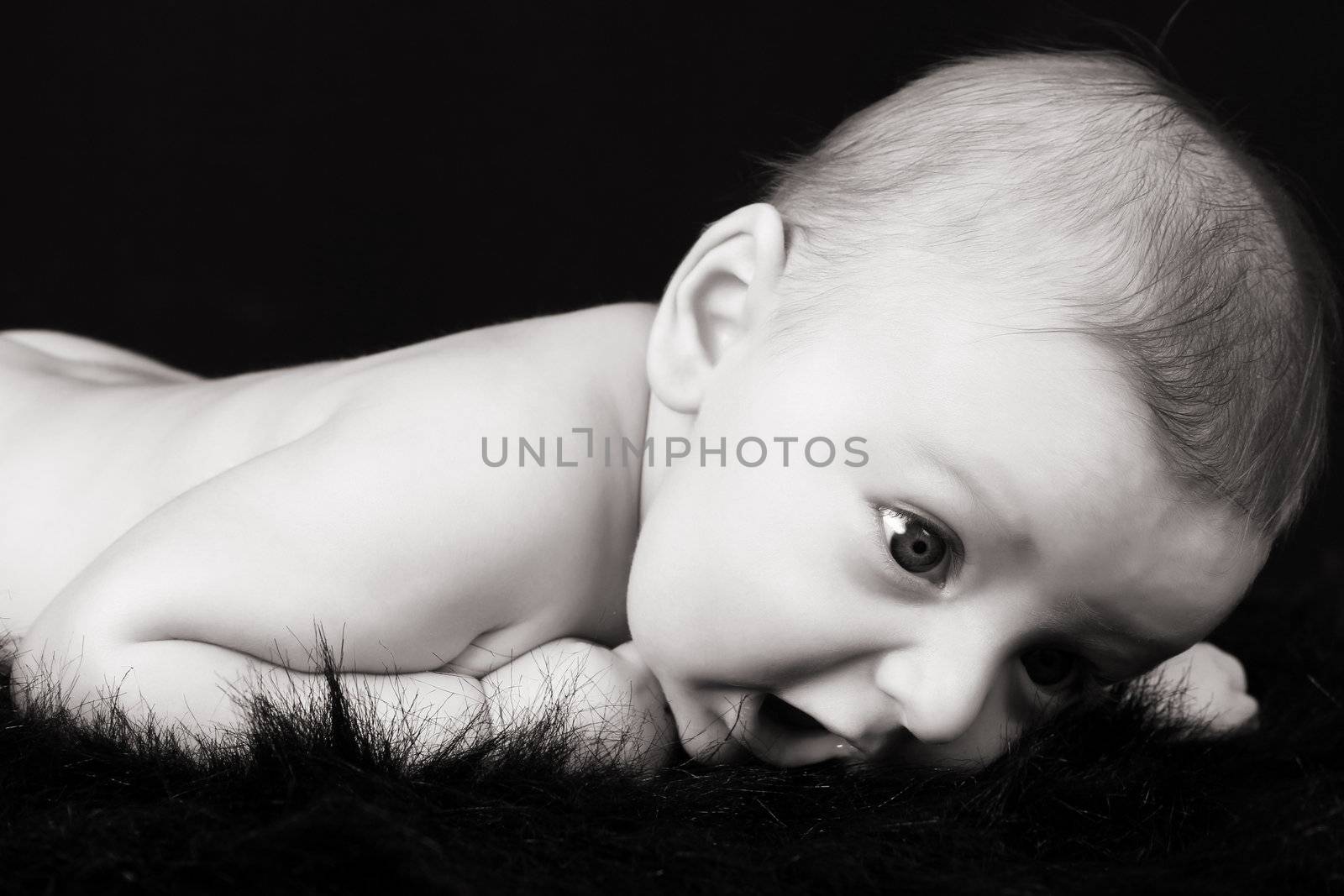 Beautiful three month old baby boy lying on black fur 