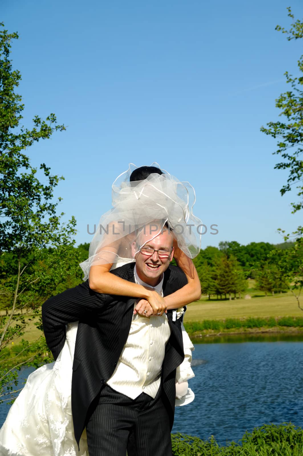Groom is lifting his bride up in a park.