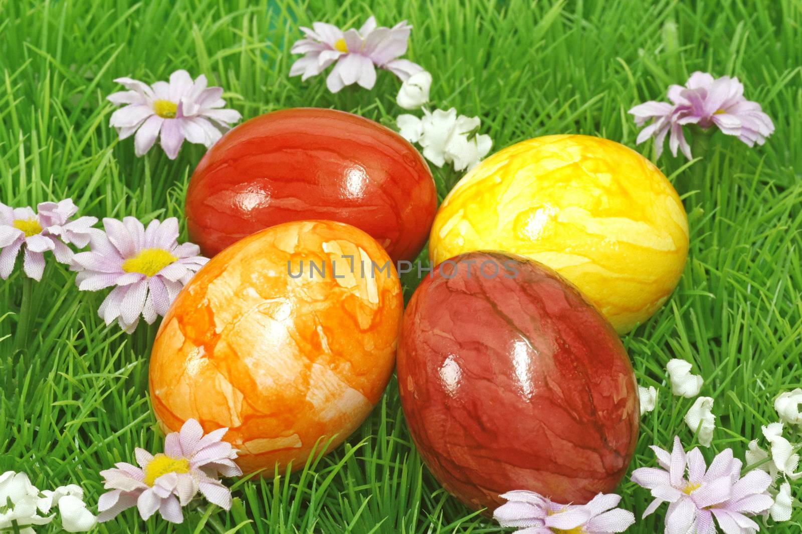 Four coloured easter eggs on grass with flowers