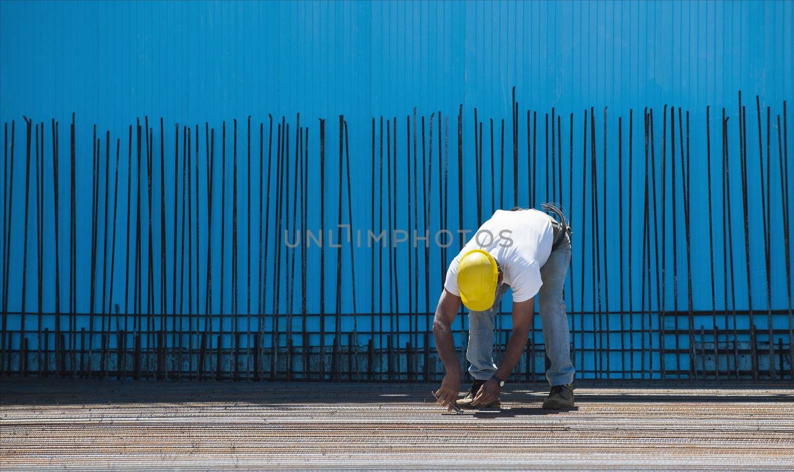 Construction worker installing binding wires to steel bars by akarelias