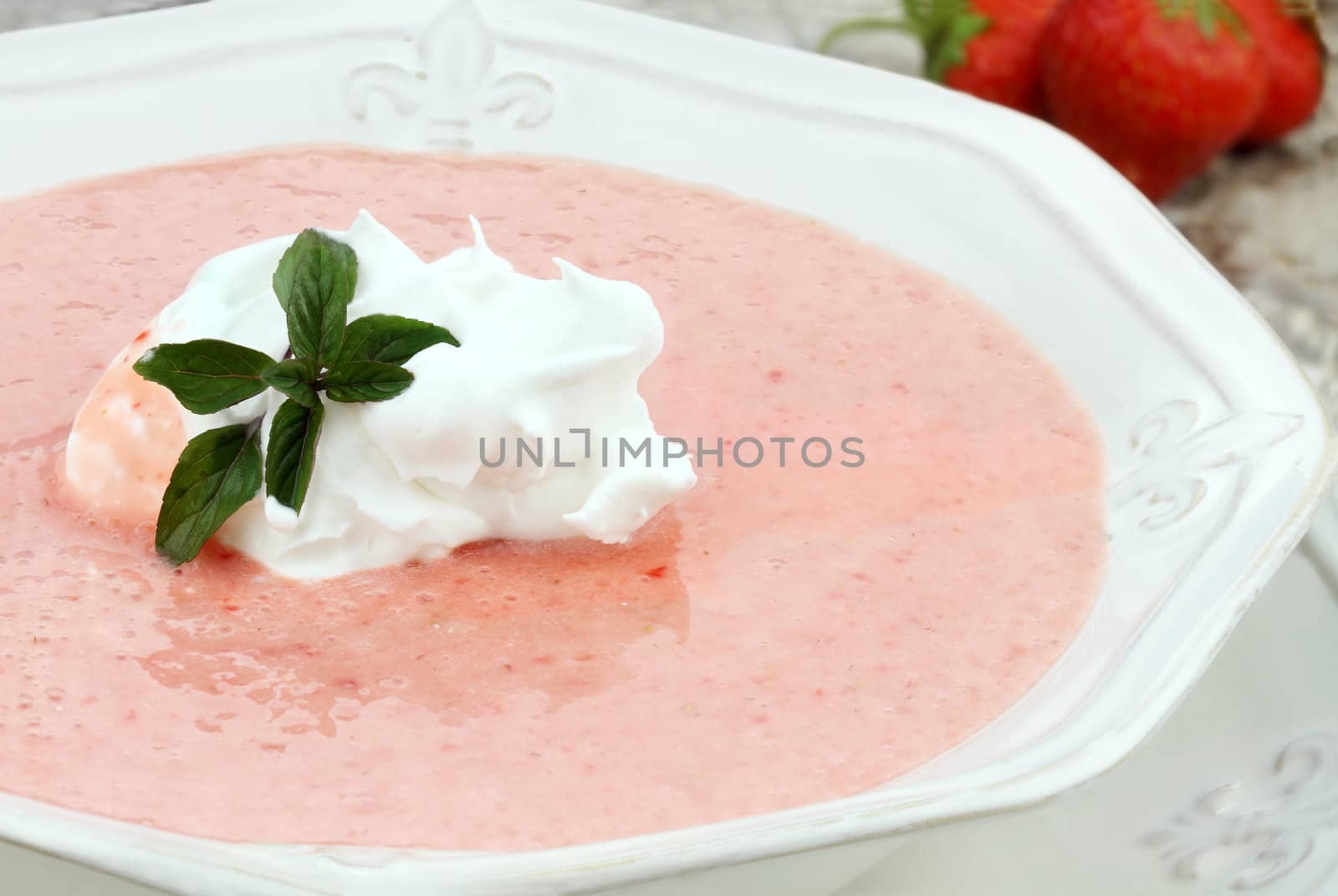 Macro of a bowl of chilled strawberry soup, garnished with a dollop of whipped cream and a fresh sprig of chocolate mint. Shallow depth of field with some blur on lower portion of image.

