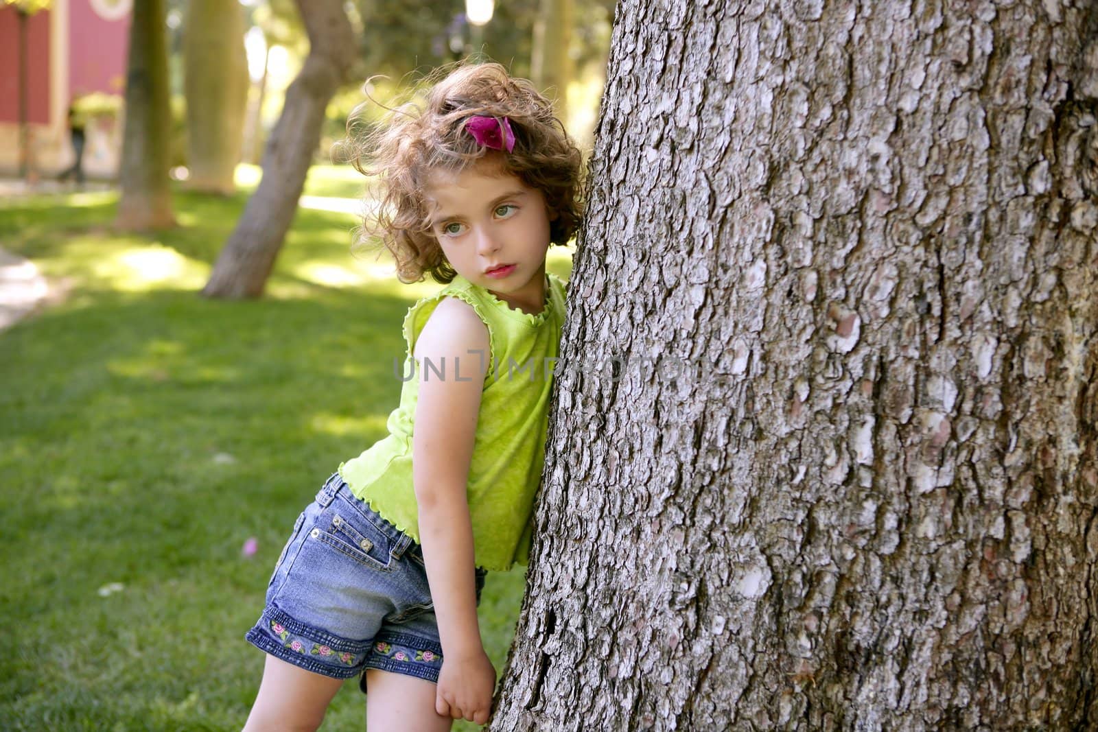Beautiful little brunette girl beside a huge pine tree trunk