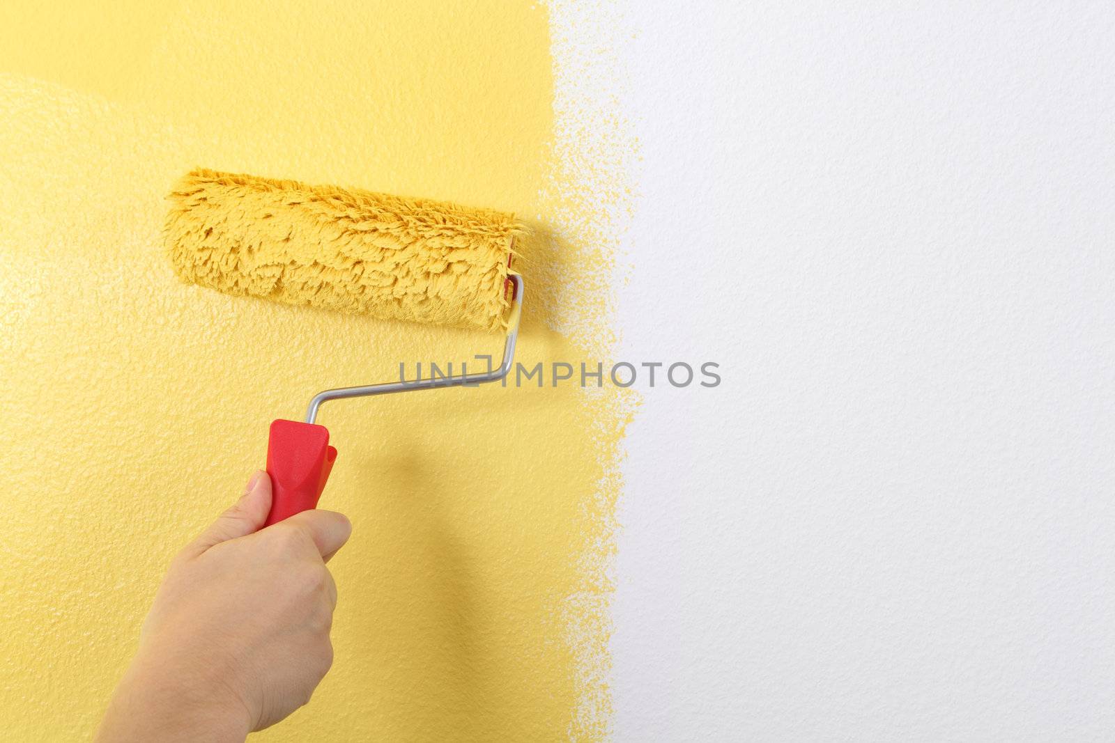 Photo of painting a wall with a roller and yellow paint.