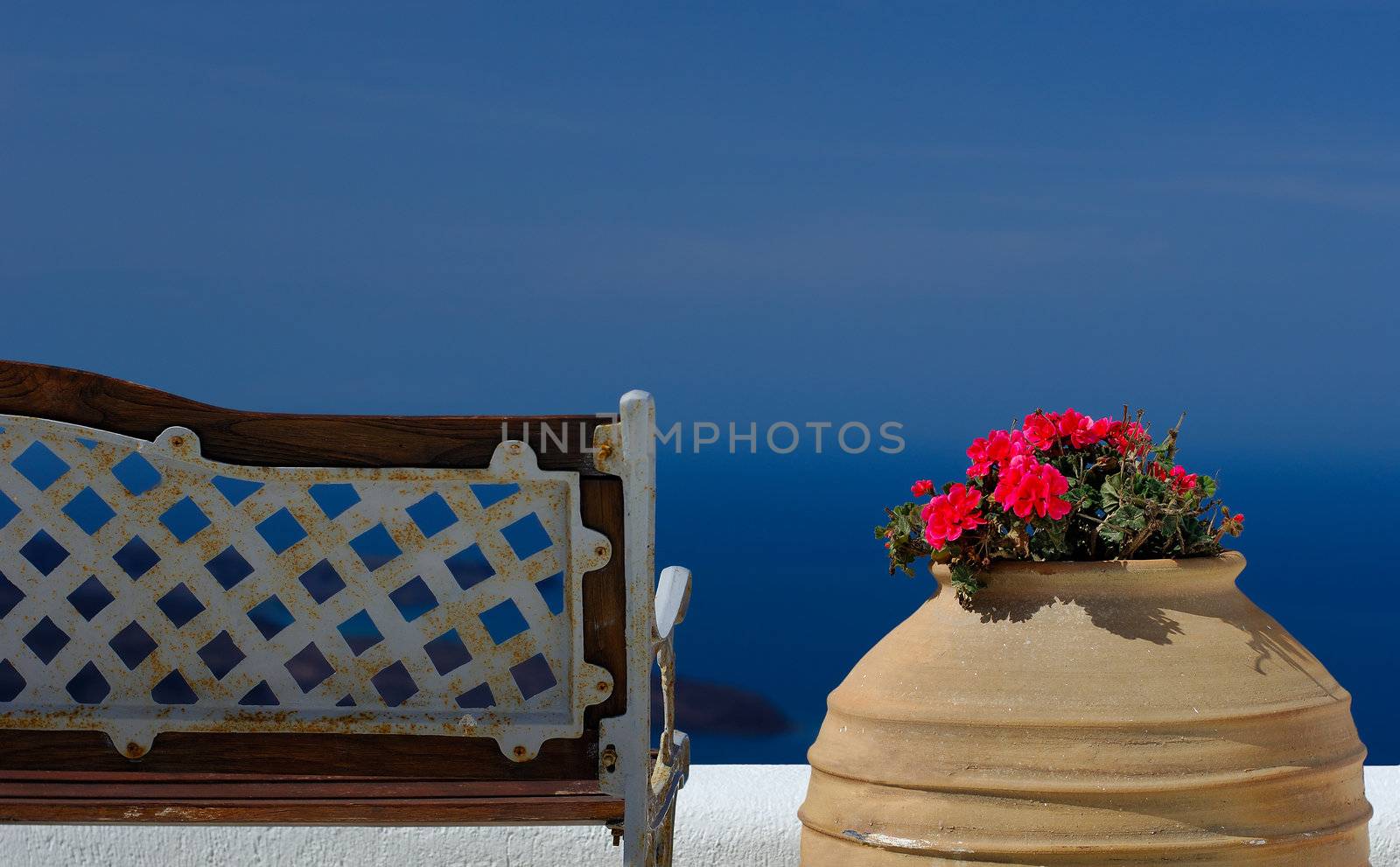 Image shows a bench and a pot with flowers on the island of Santorini overlooking the magnificent view