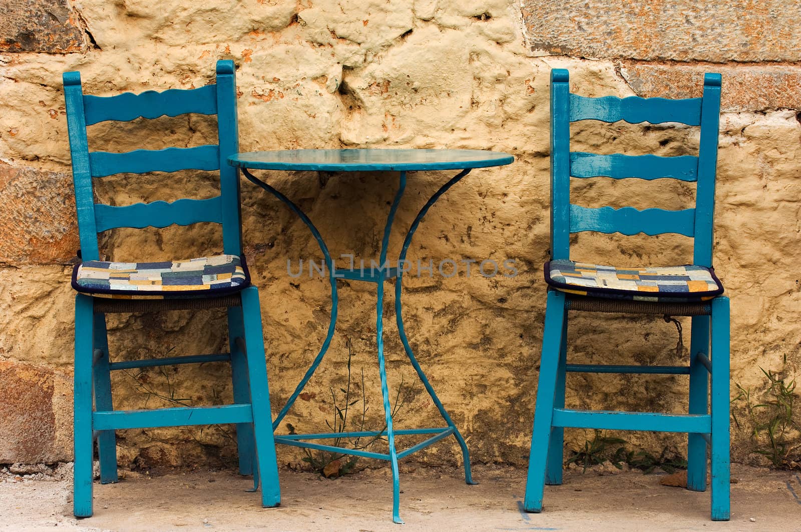 Blue table and chairs in a country coffee shop, against a highly textured wall. Image captured in southern Greece.