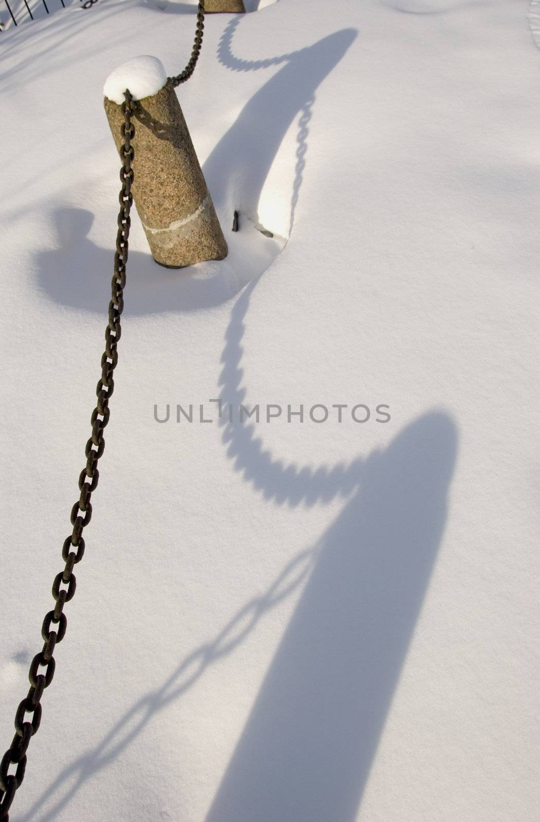 Shadows of decorative fence with chains covered with deep winter snow.