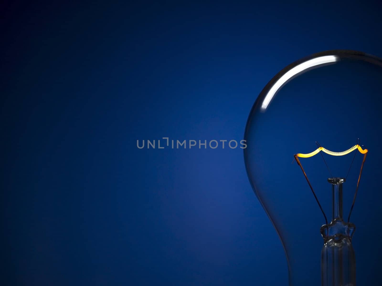 Close up on a turned on light bulb over a blue background. Copy space.