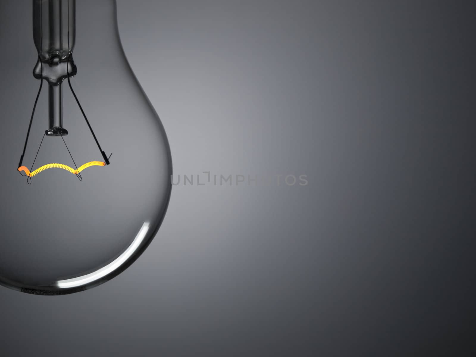 Close up on a transparent light bulb over a grey background. Copy space.