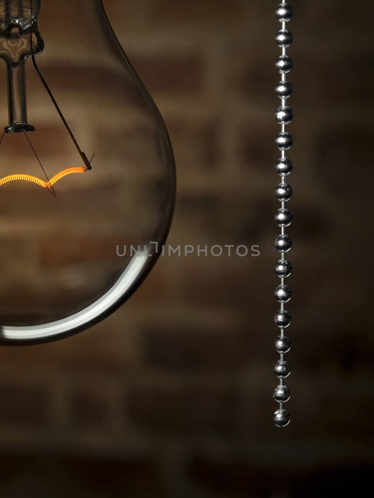 Close up on a transparent light bulb with a pull switch over a brick wall background.