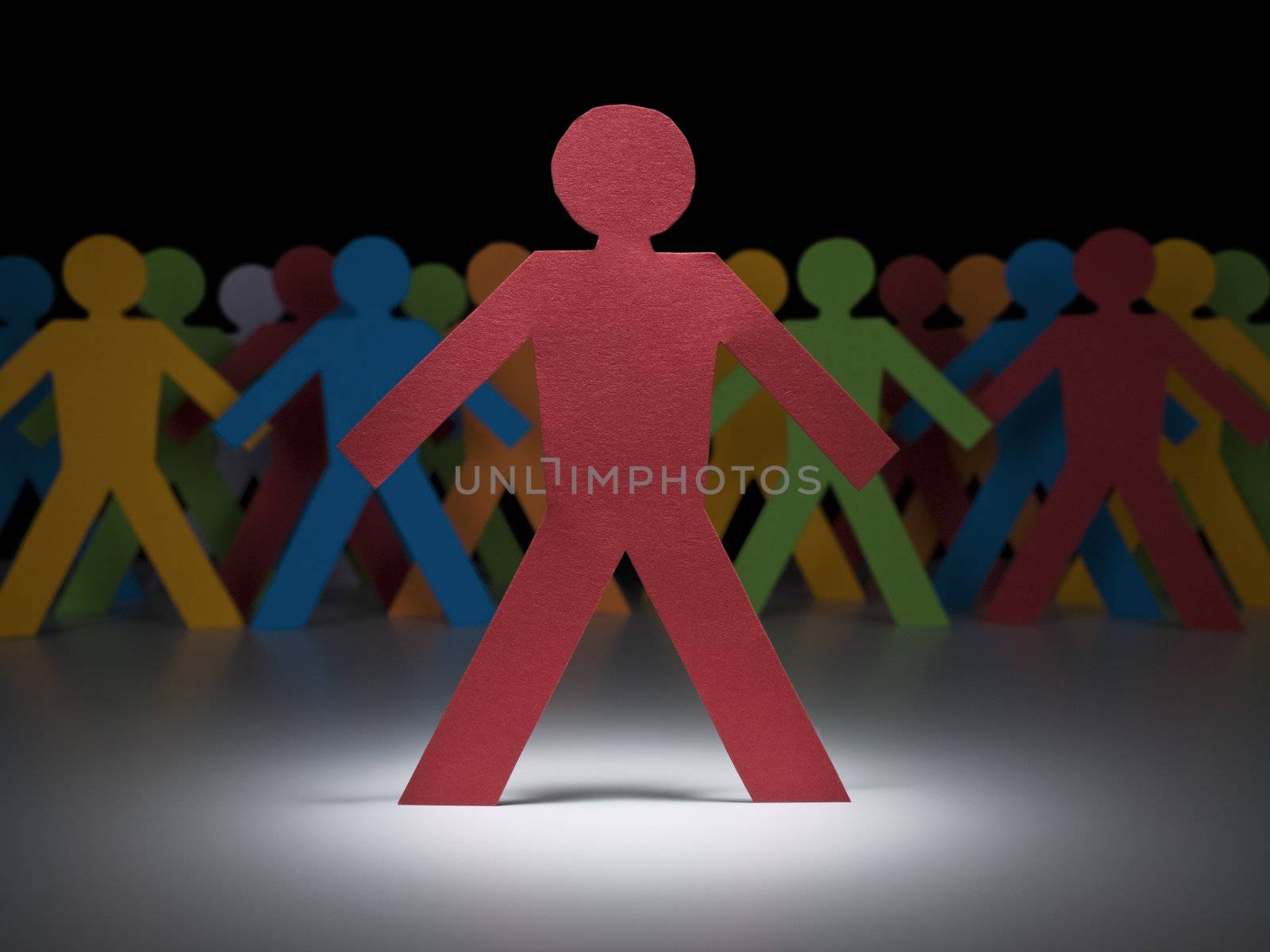 A red paper figure stands under the spotlight in front of multicolor crew.