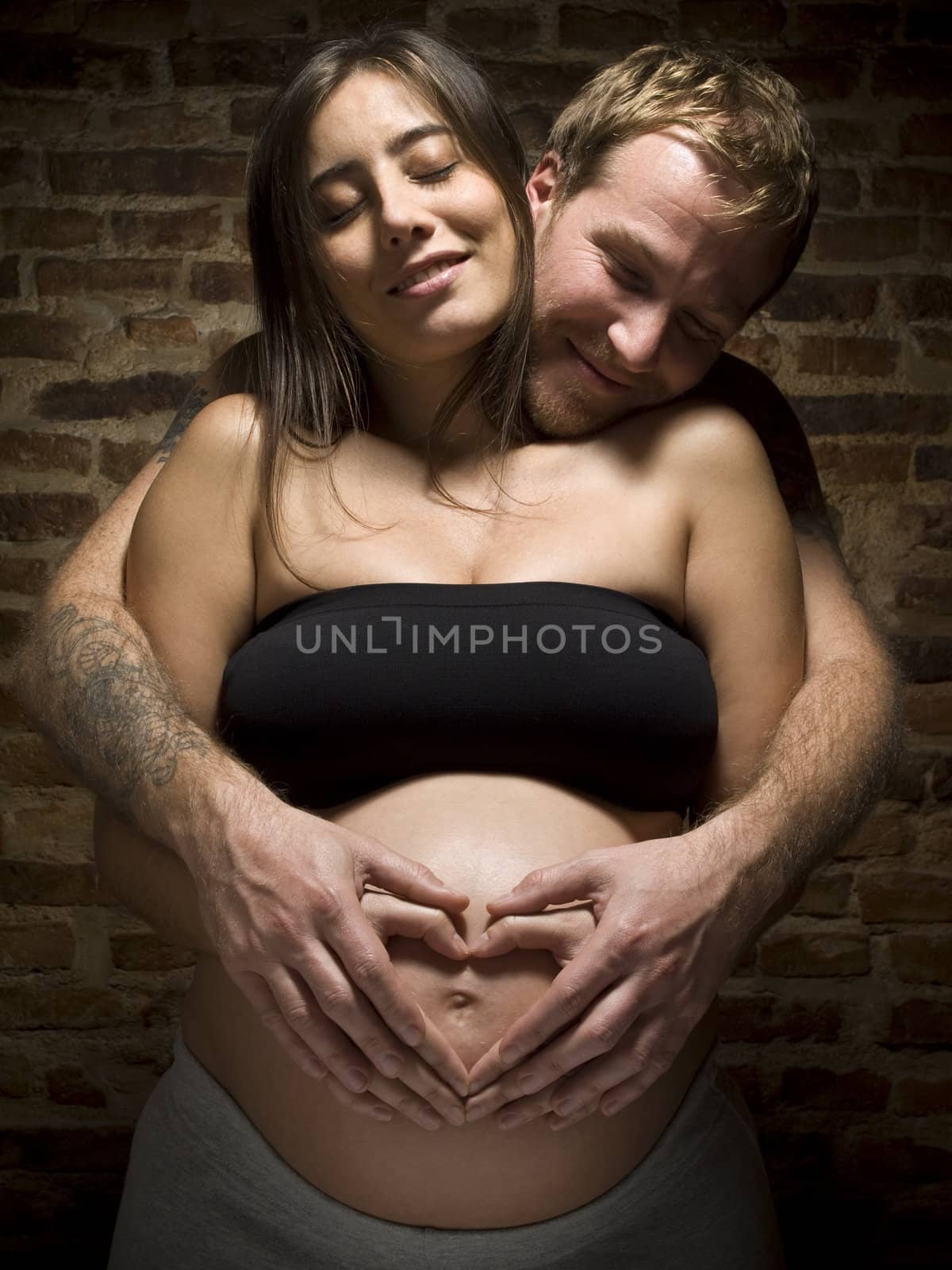 A young couple holding the pregnant belly and making a hard shape with their hands.
