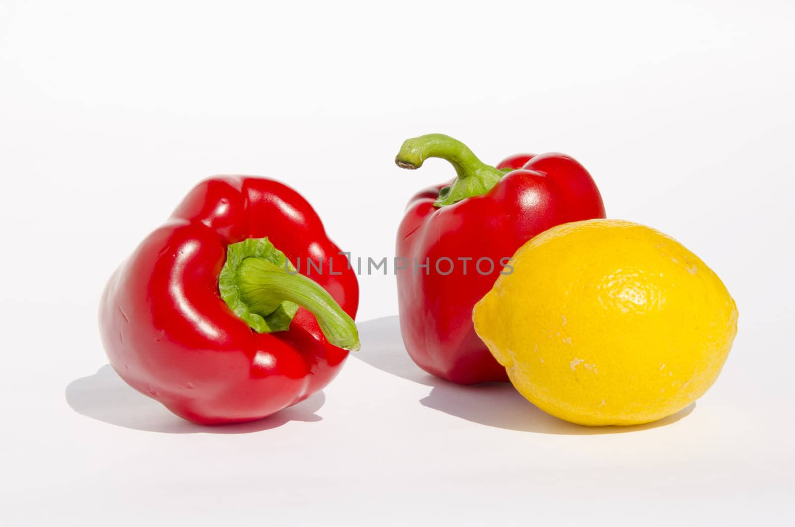 Few red paprikas and one yellow lemon with shadows on a white background.