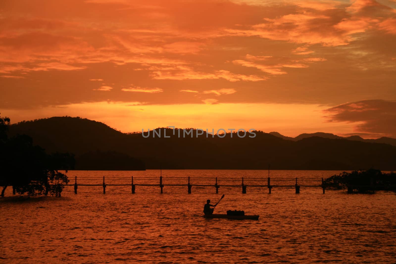 orange sunset with silhouettes of mountain, bridge and boat 
