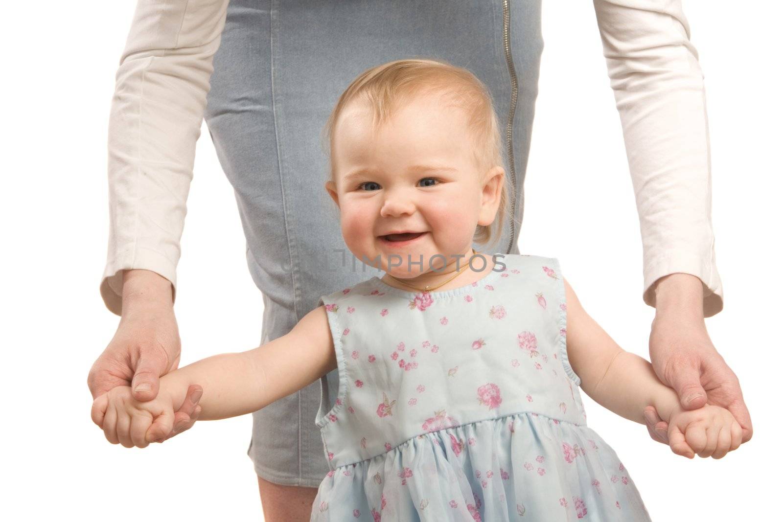 The smiling little girl in a blue dress hold on mum's hands and tries to go
