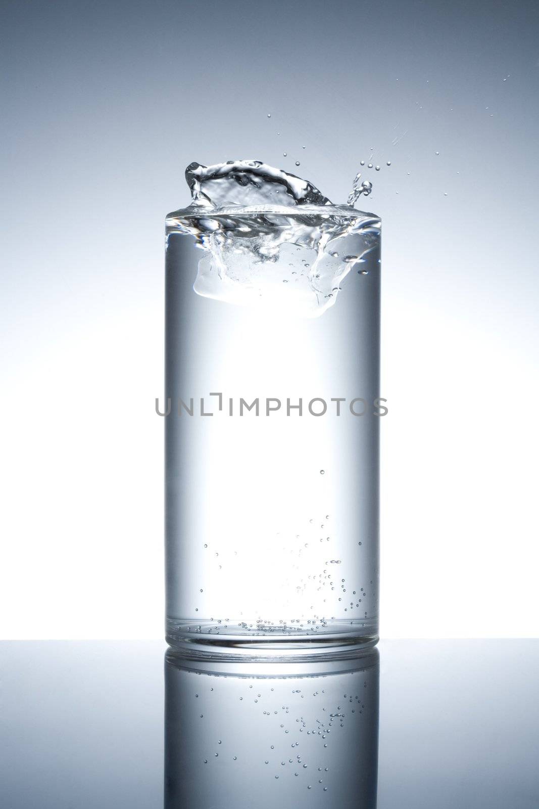 Glass filled with water with splash on a reflecting surface
