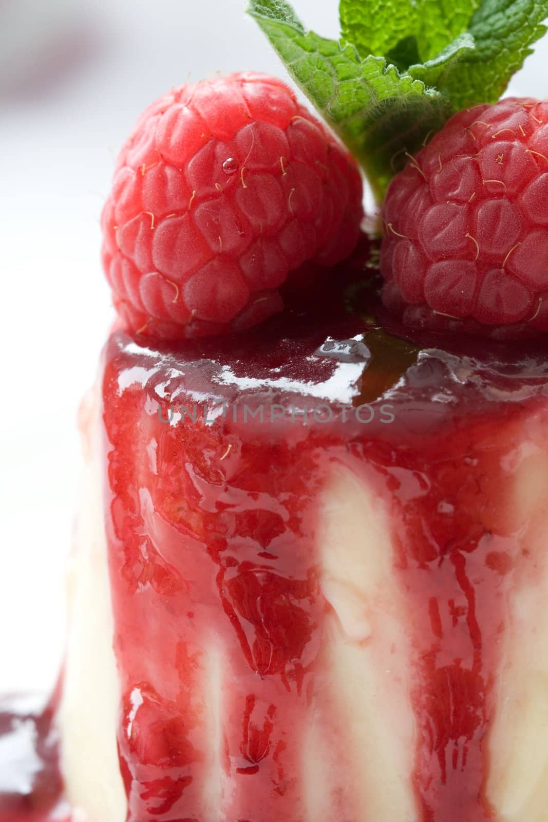 Small pannacota dessert covered in raspberry sauce and fresh raspberries topped with a few fresh mint leaves