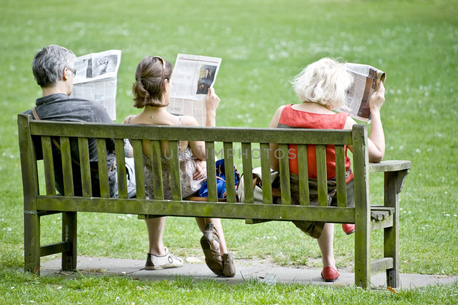 Three people on a garden bench read newspapers, taken in London on April 2011 