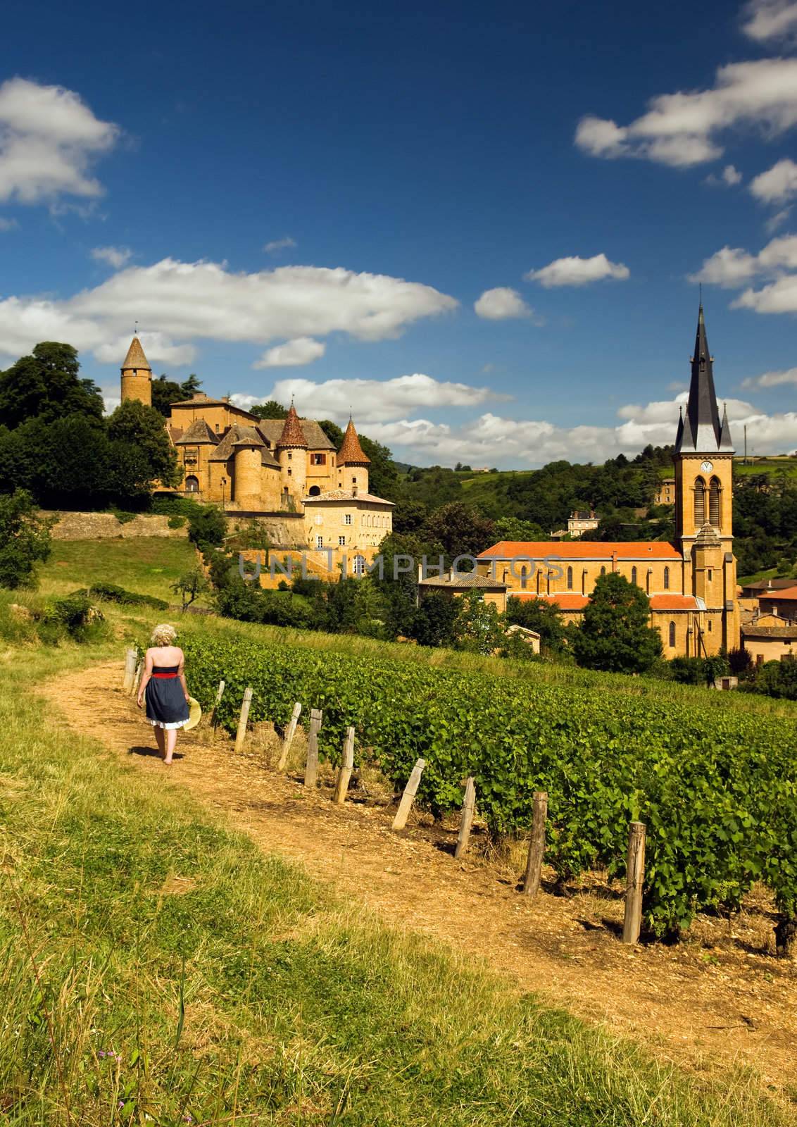 Image shows a blond country girl walking on a gravel road in a village in the French wine-making region of Beaujolais