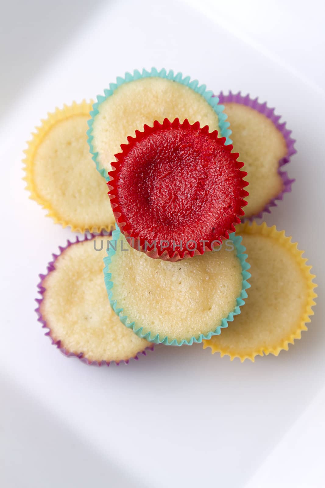 Plate of small undecorated cupcake in multicolored paper cup
