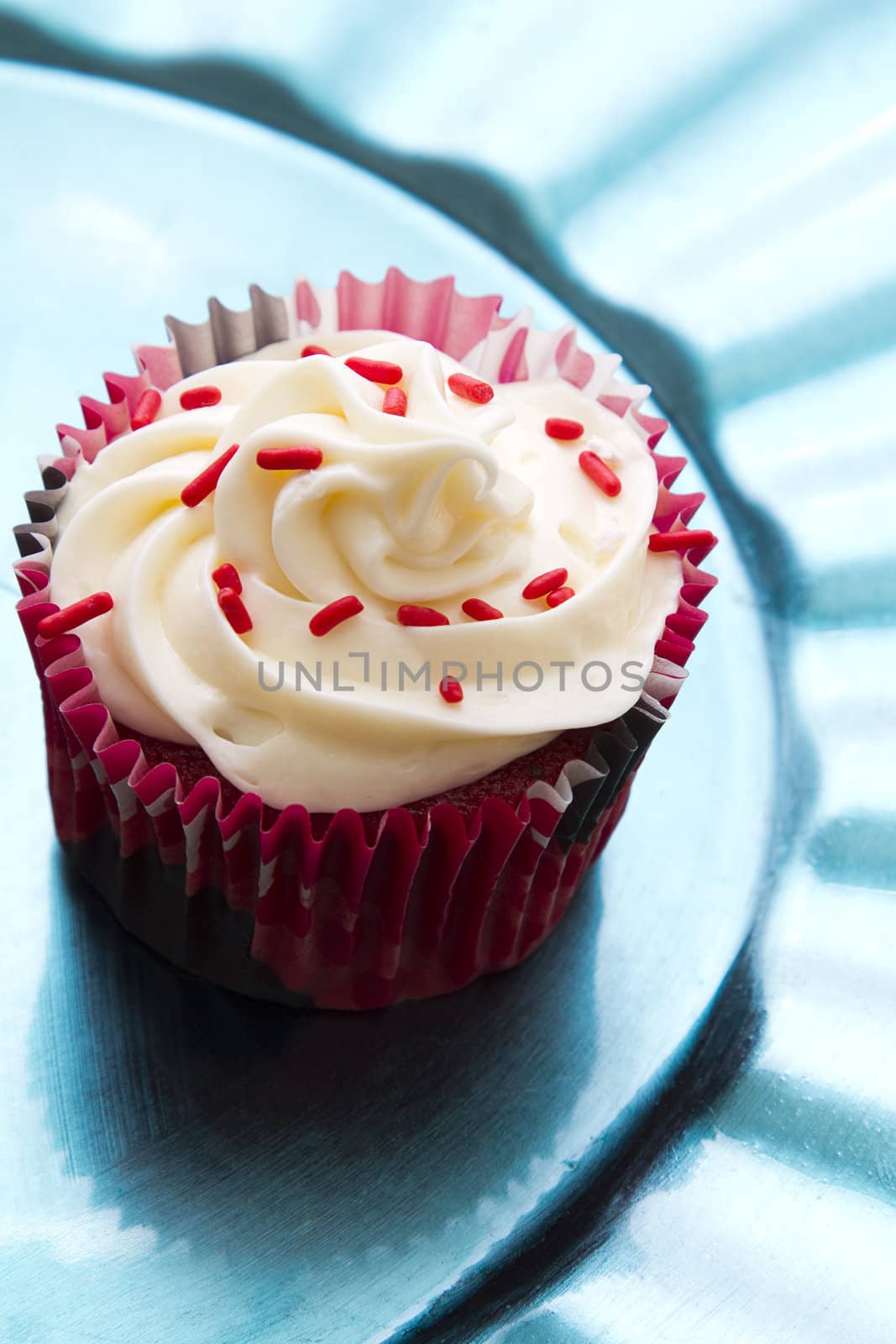 cupcake with white frosting and red sprinkle on turquoise plate