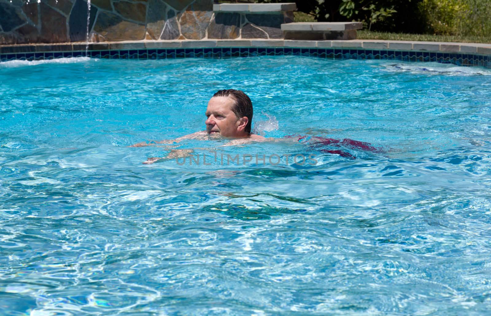 Baby boomer male swimming across a backyard swimming pool on a hot summers day