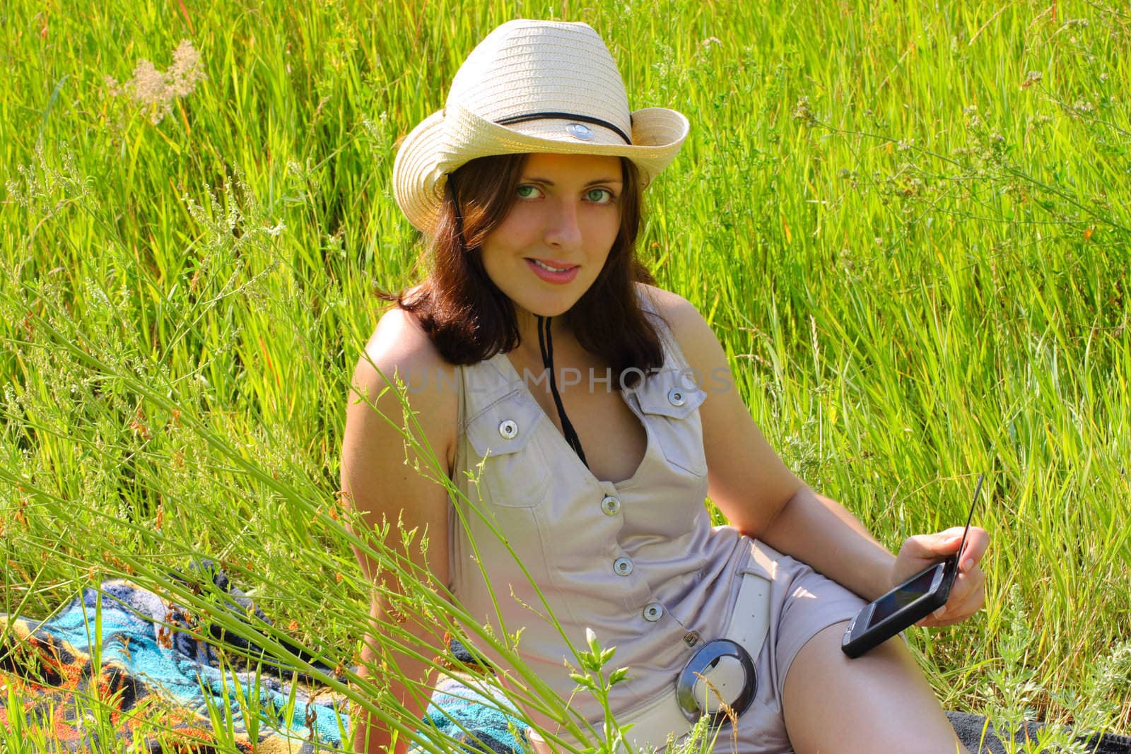 The girl sitting on a summer meadow with handheld