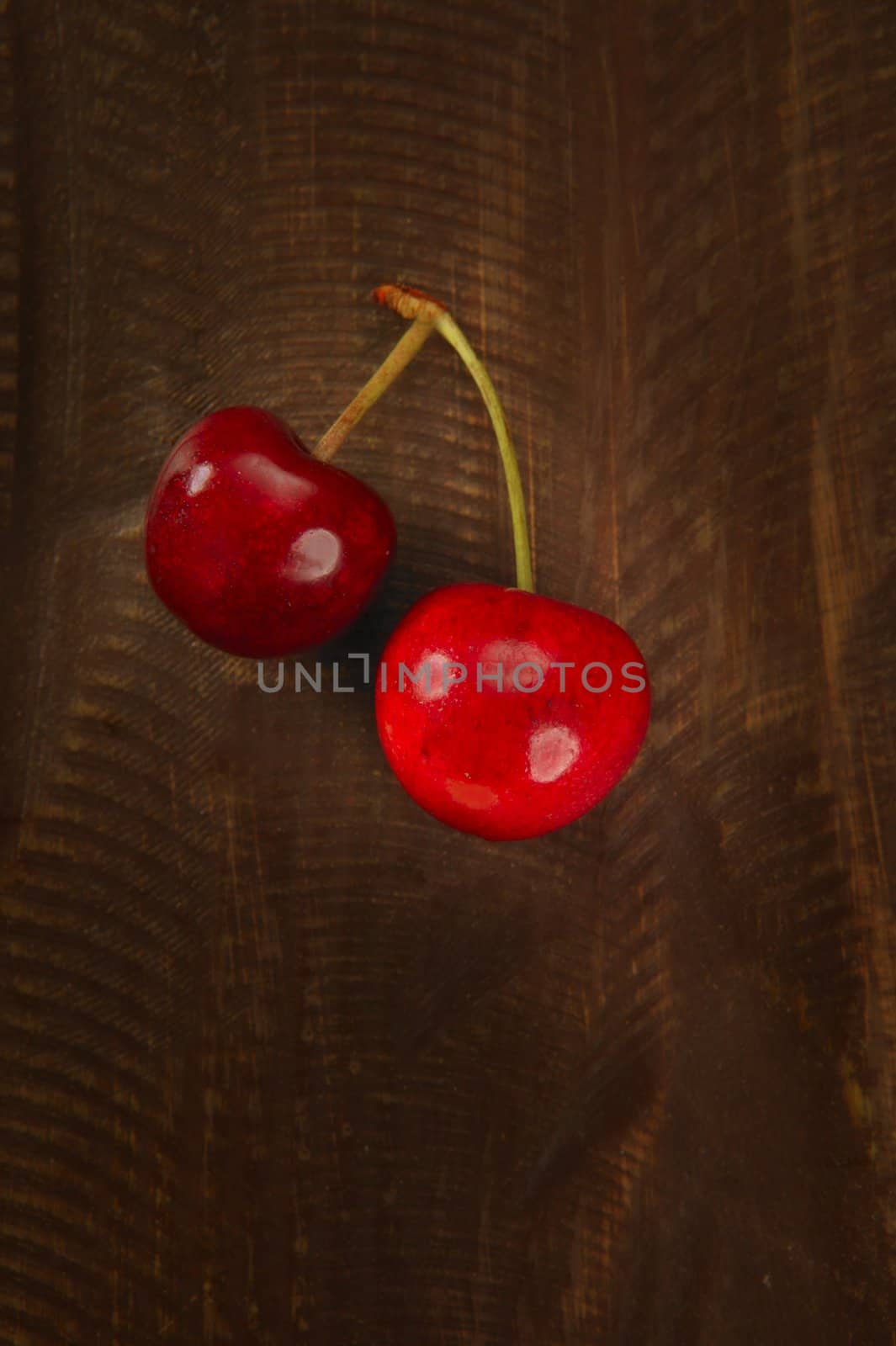 Two cherry red fruits over dark wooden background