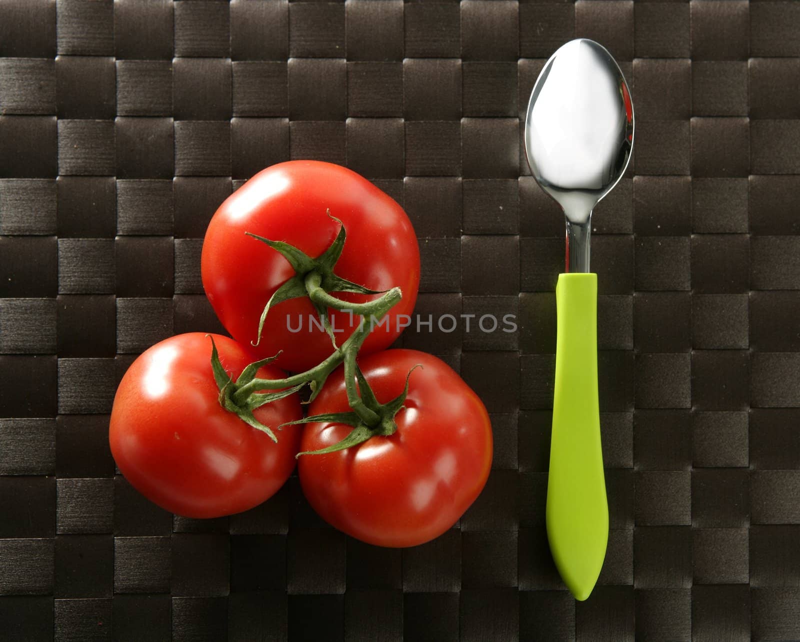 Three red tomatoes in the same one branch with a vibrant green spoon