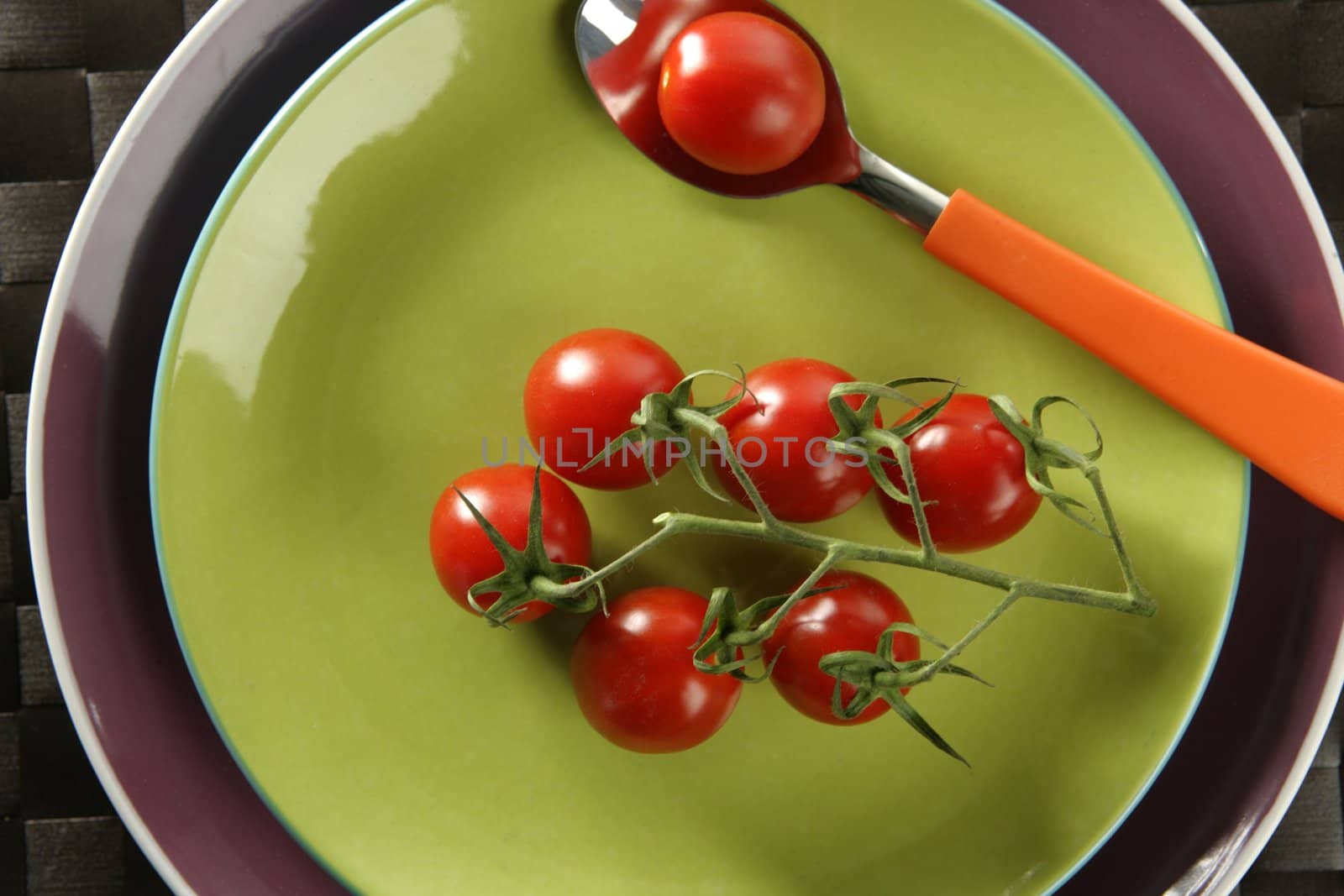 Red cherry tomatoes branch, spoon and a green dish by lunamarina