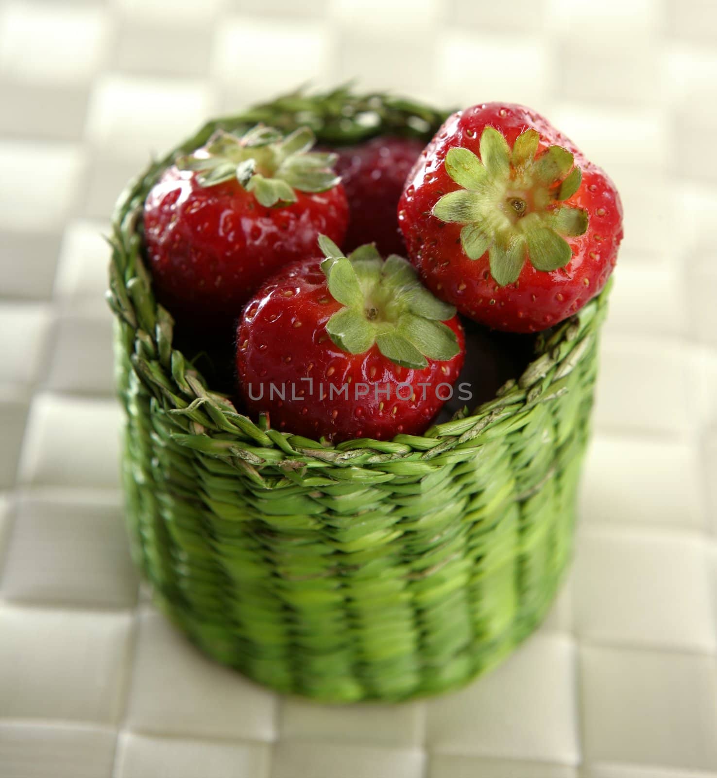 Strawberries in a green little basket over white tablecloth