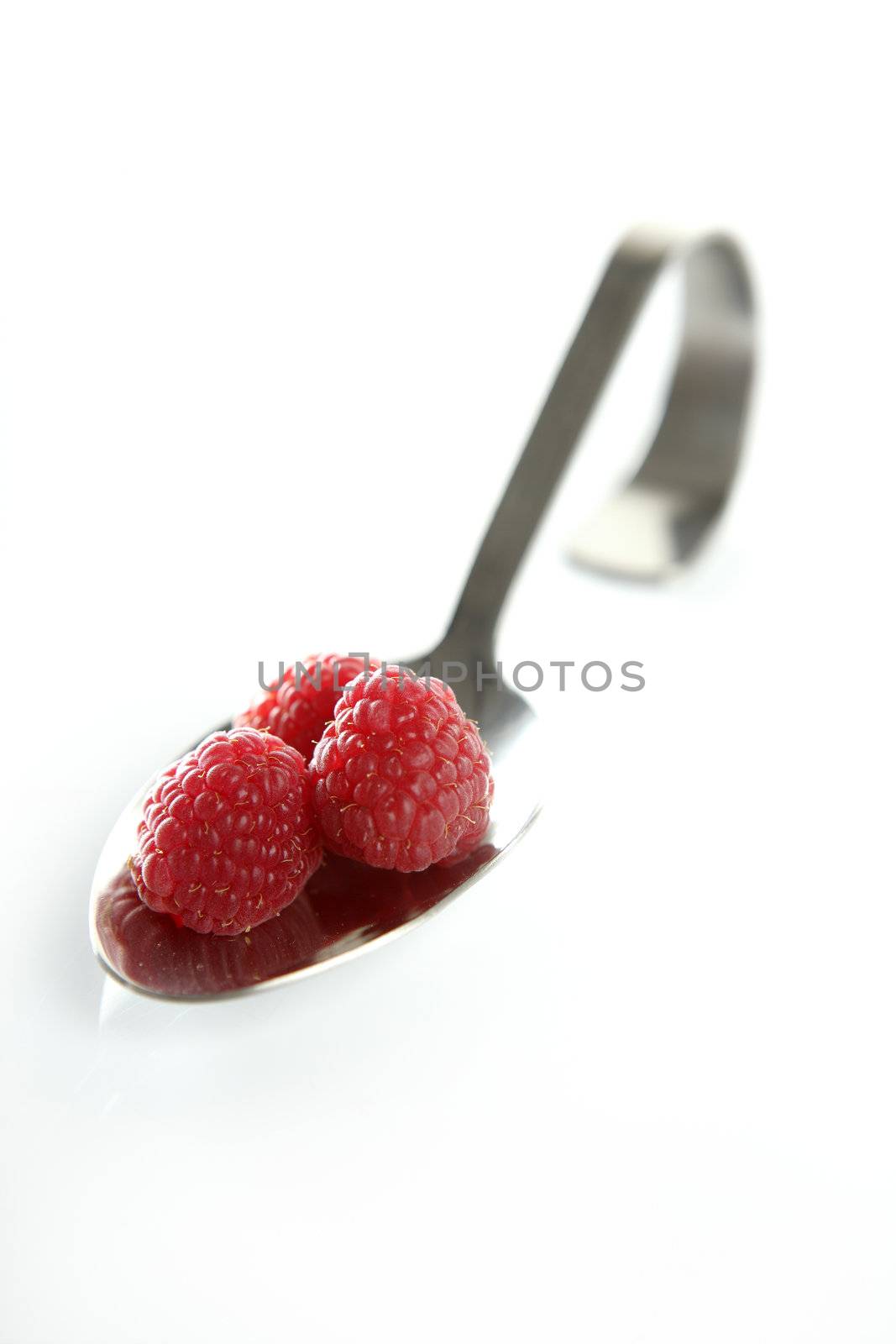Raspberries in a curved spoon in white background