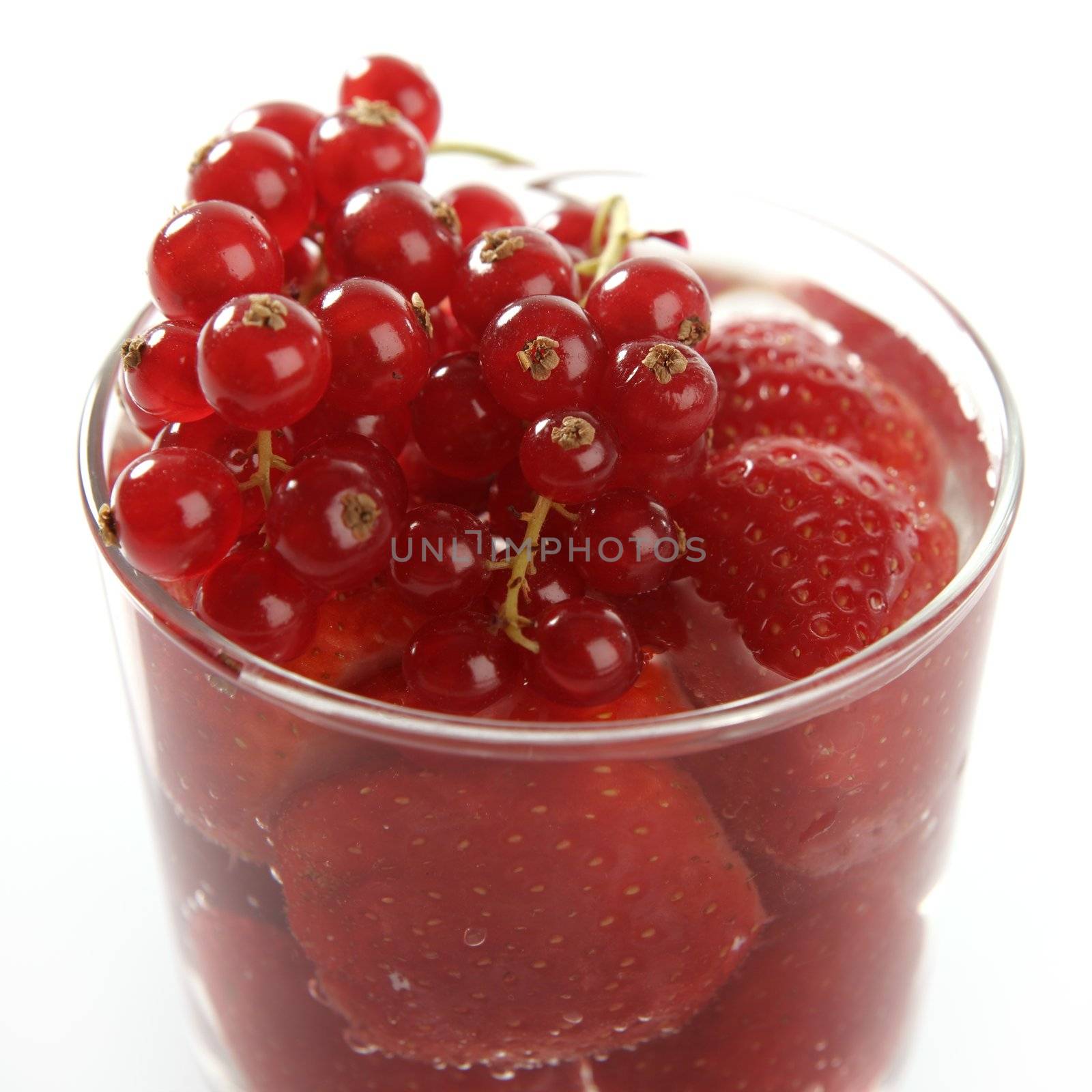 Glass cup full of strawberries and redcurrant at studio in white background
