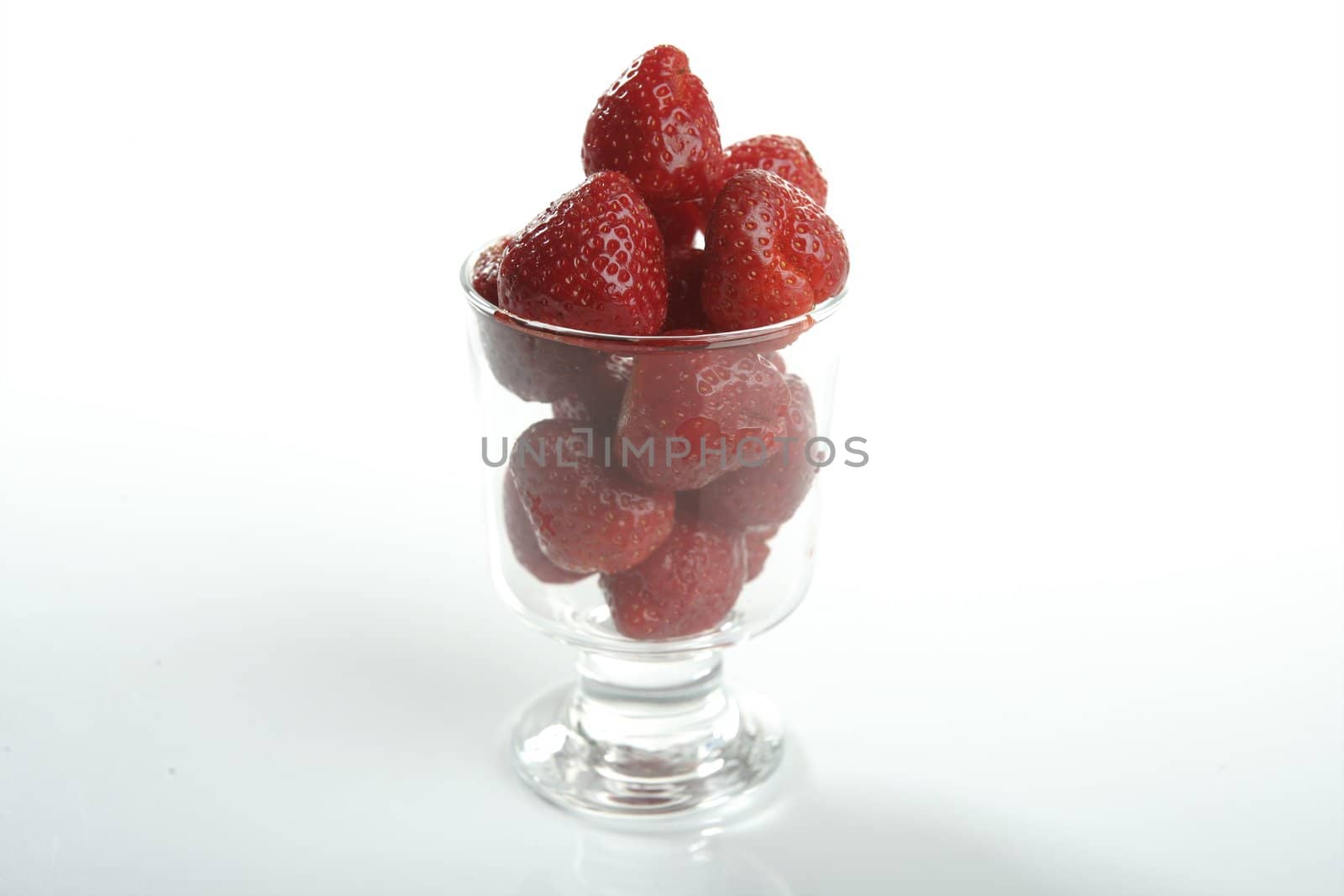 Glass cup full of strawberries in studio white background