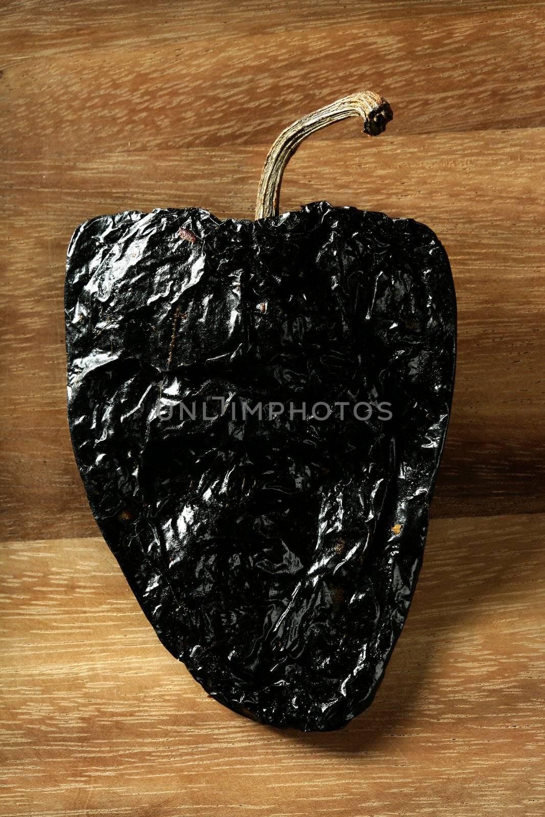 One black mexican dried chili pepper still on warm wood background