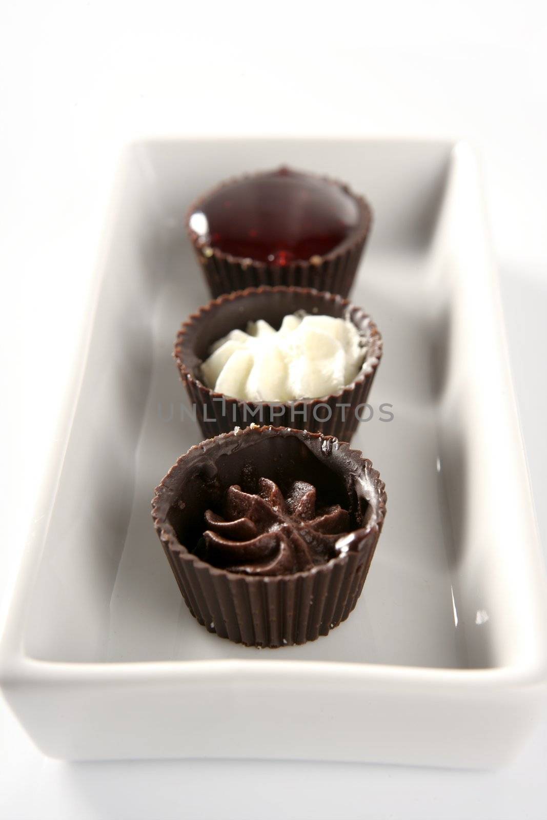 Three little chocolate cakes in a line with cream and strawberry jam