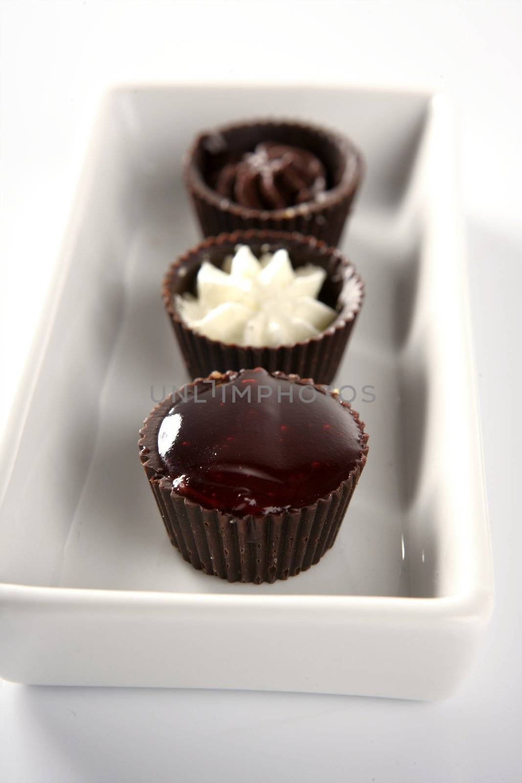 Three little chocolate cakes in a line with cream and strawberry jam