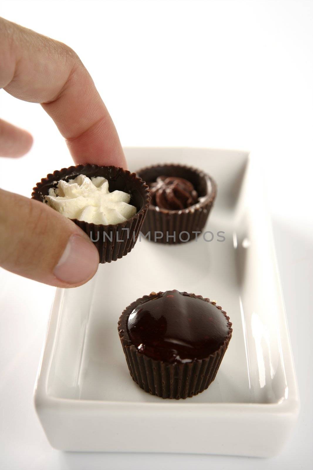 Three little chocolate cakes with cream, strawberry jam and human hand