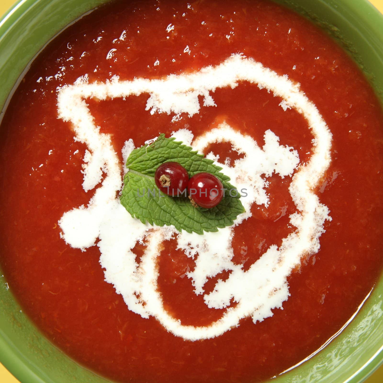 Mediterranean tomato soup with basil and redcurrant in a colorful green dish over wood