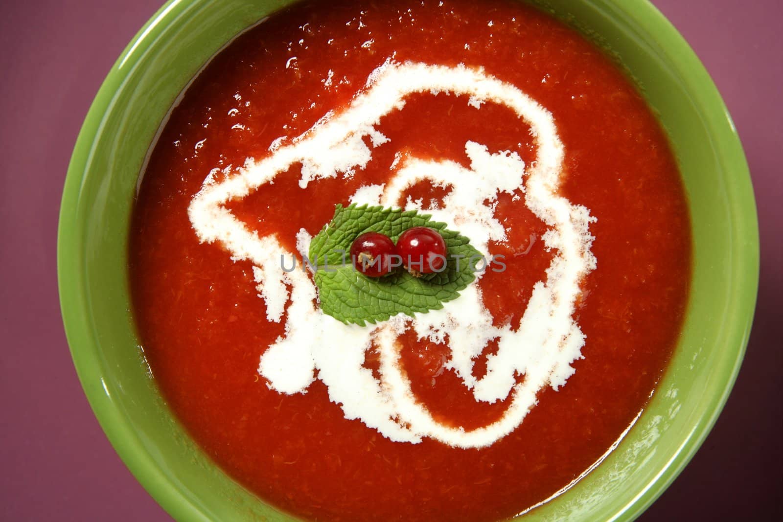 Mediterranean tomato soup with basil and redcurrant in a colorful green dish over wood