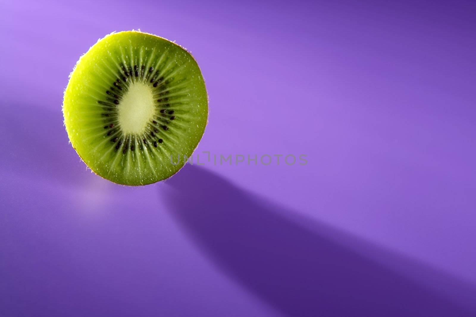 Green Kiwi slice over vivid purple background, copy space