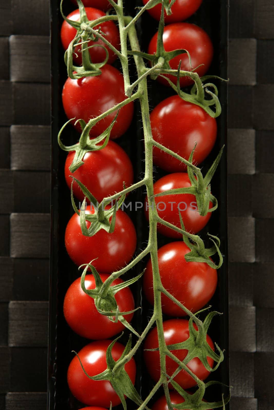 Red tomatoes branch un a black plastic box over brown tablecloth
