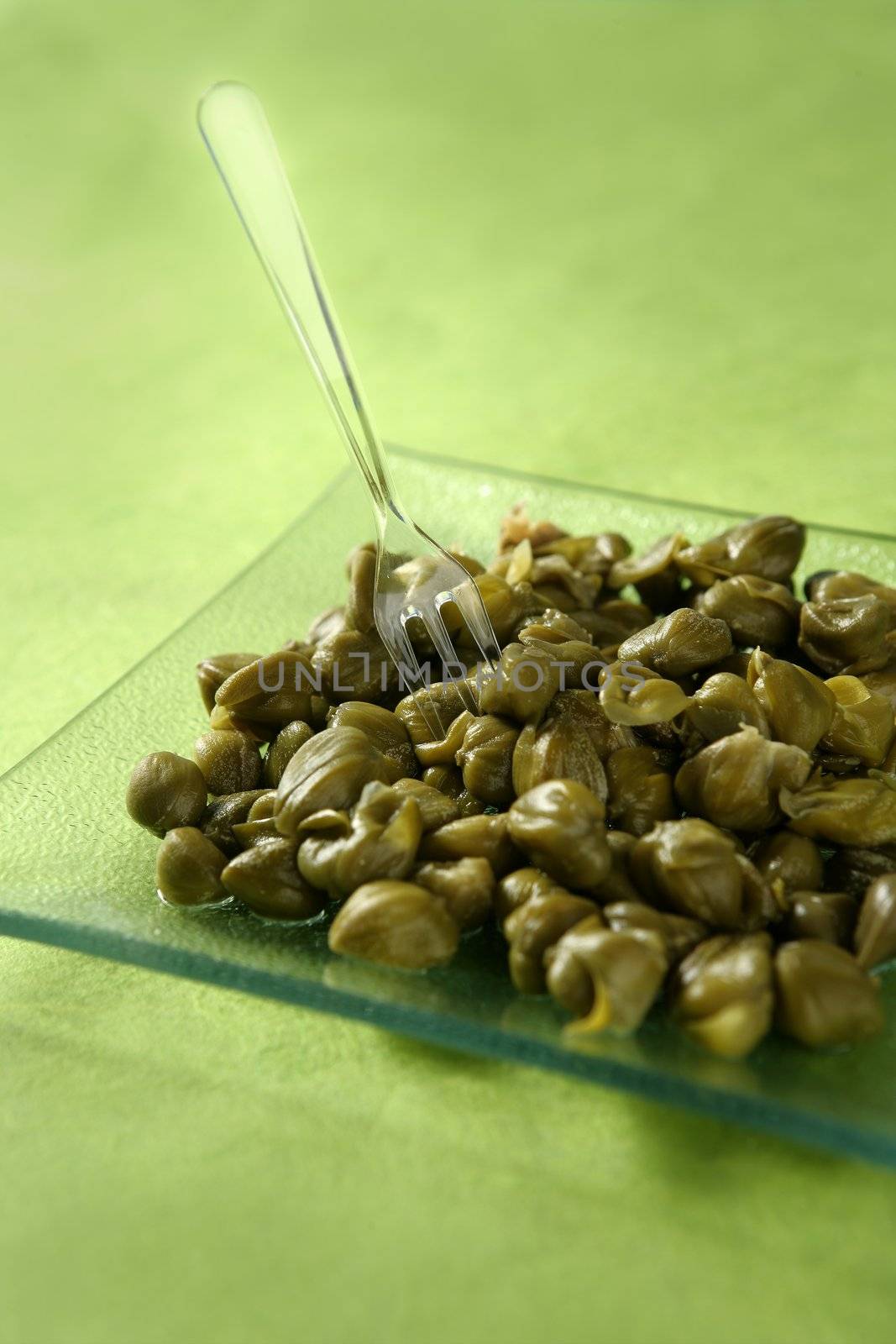 Capers with vinegar snack on a transparent plate, green background