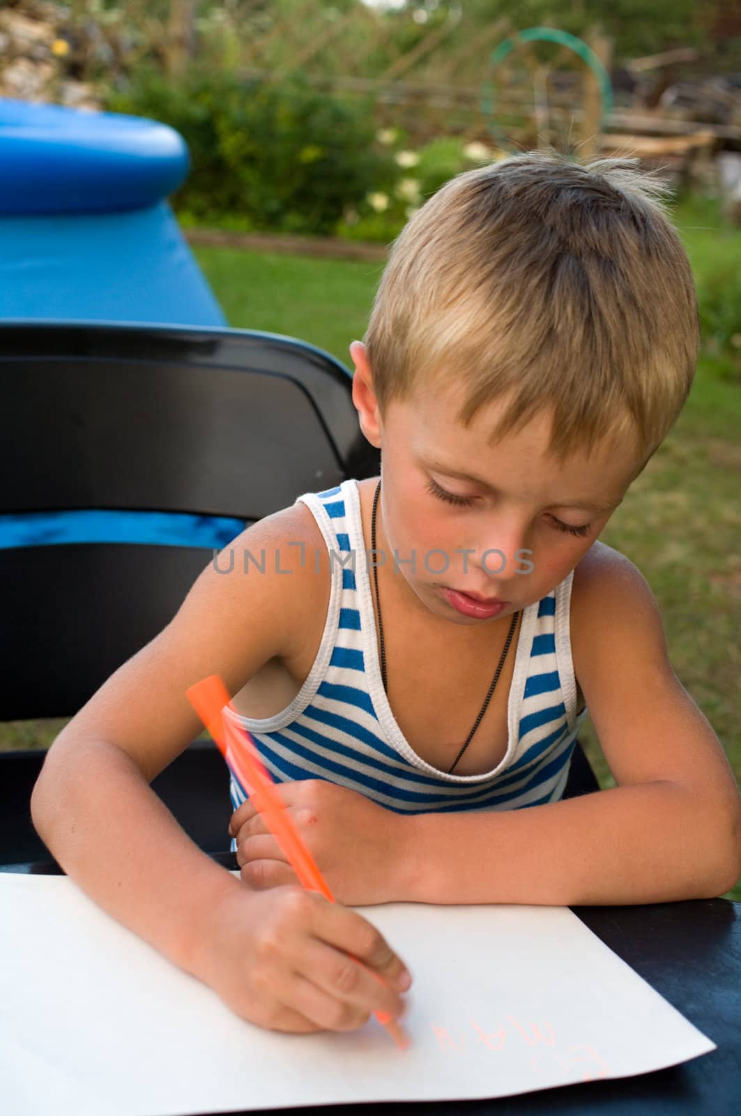 The fair-haired boy writes on a sheet of paper a pencil.