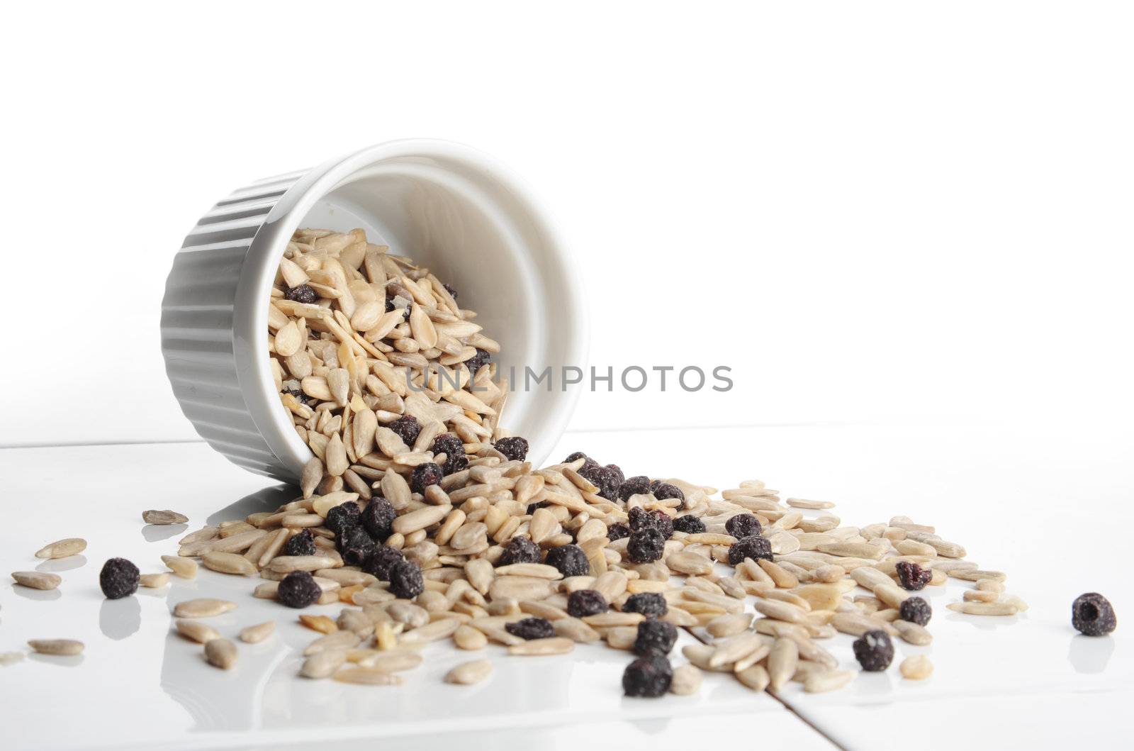 Sunflower seeds and raisins in a small white cup and scattered on a ceramic table