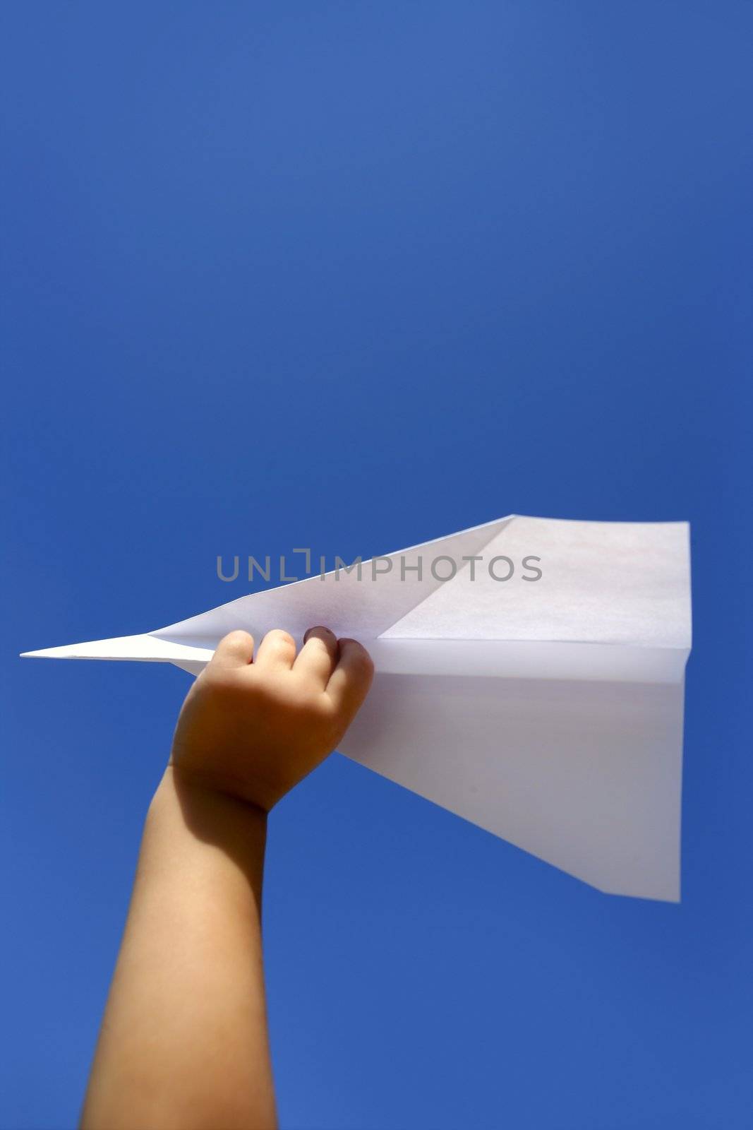 Paper airplane in children hand over sunny summer blue sky