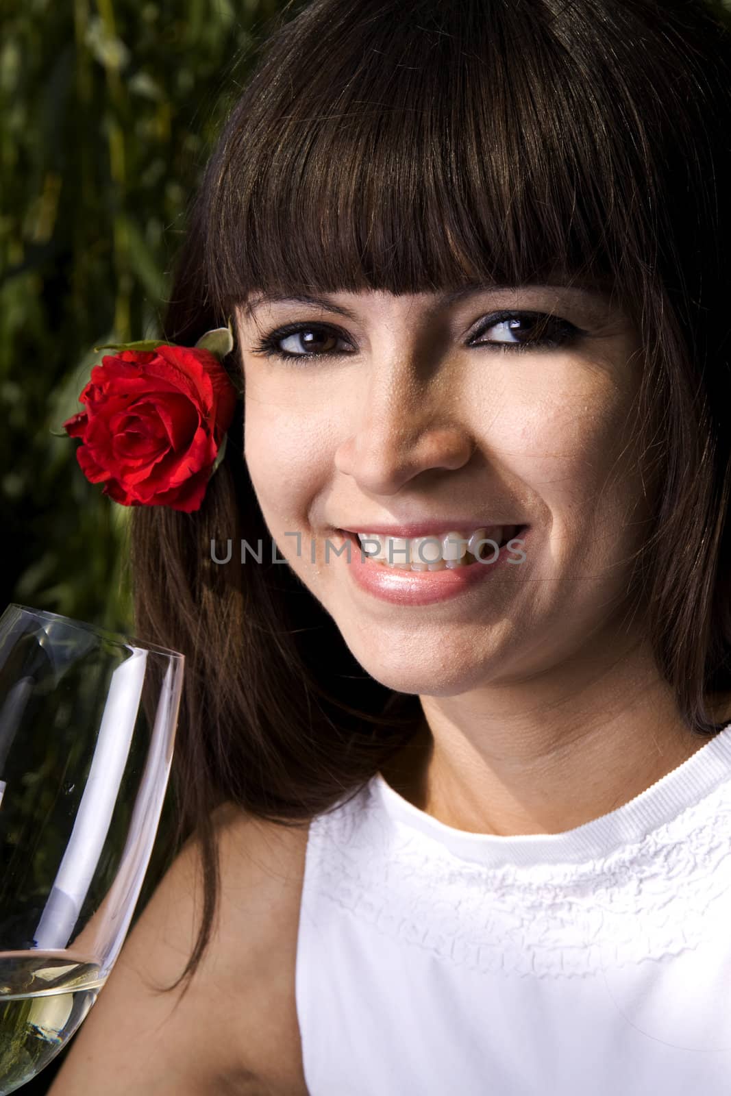 Beautiful brunette with a rose in her ear is enjoying white wine