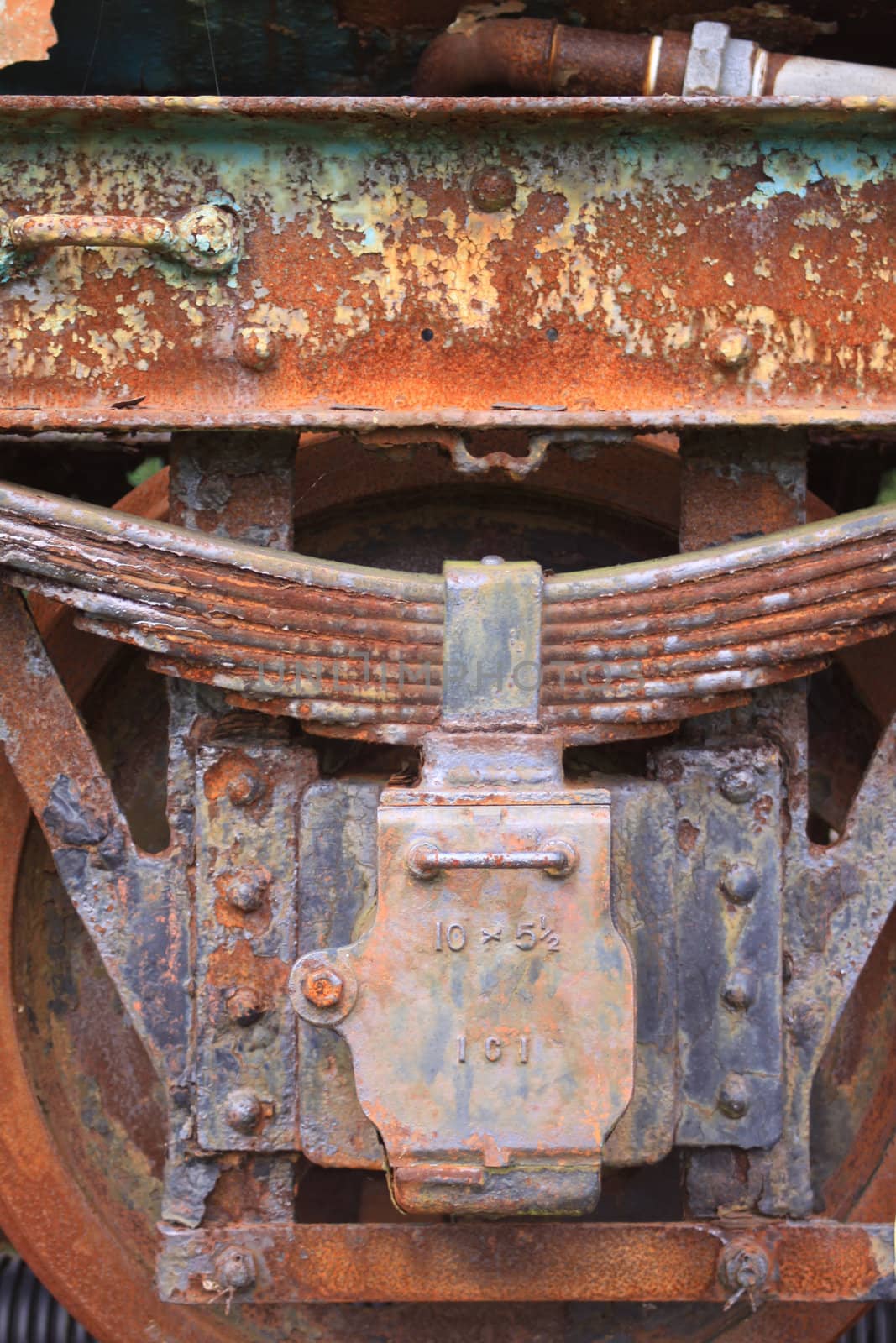 Close up detail of a rusty and peeling bogie from a derelict train carriage. Detail shows wheel and rusty suspension blocks.