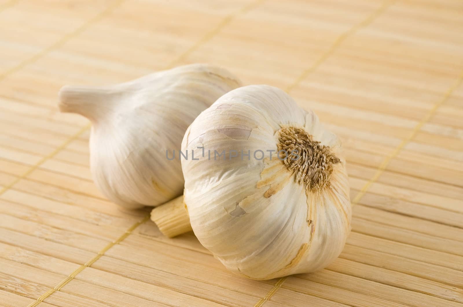 Two garlic heads on a bamboo mat, studio shot.