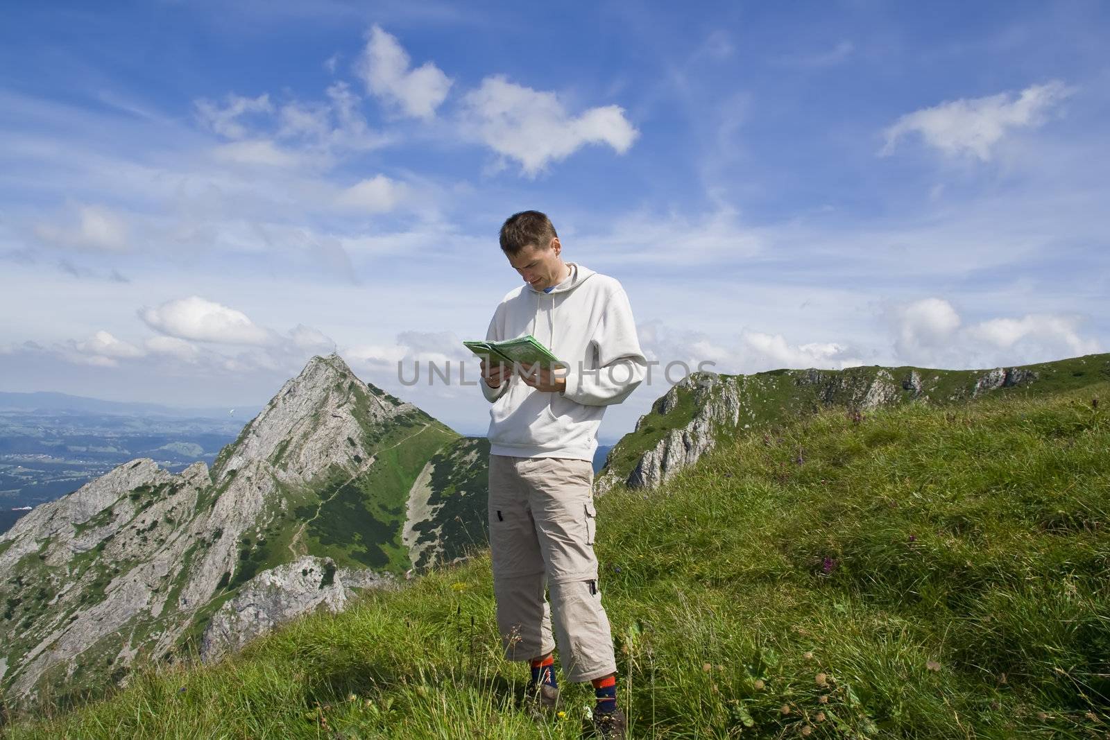 Mountain tourist looking into map over blue sky by Adiasz
